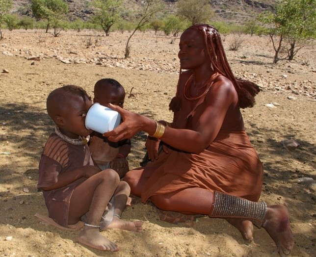 Himba woman gives water to a child.
